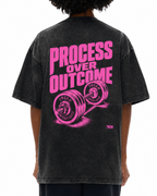 A person shown from the back wearing a faded black graphic T-shirt with bright pink text reading 'PROCESS OVER OUTCOME' and a pink barbell illustration, paired with dark pants against a plain white background.